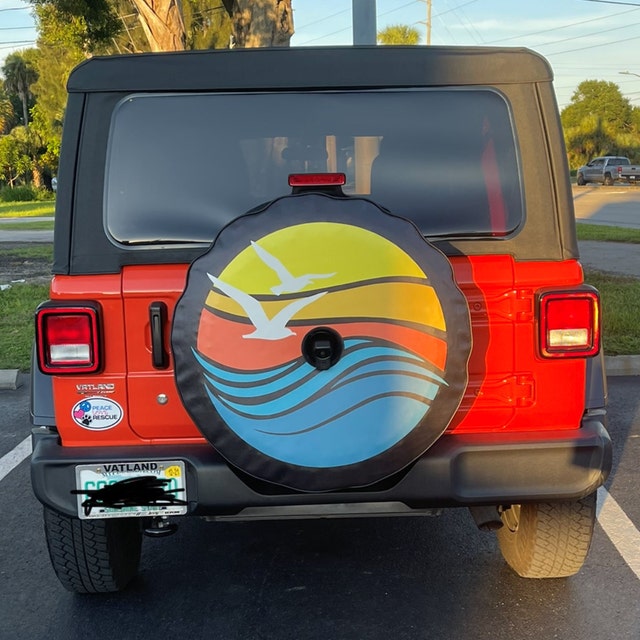 Red Jeep Wrangler and a custom spare tire cover design of geometric beach waves and sunset with seagulls flying. Red Jeep Wrangler spare tire cover with camera hole.