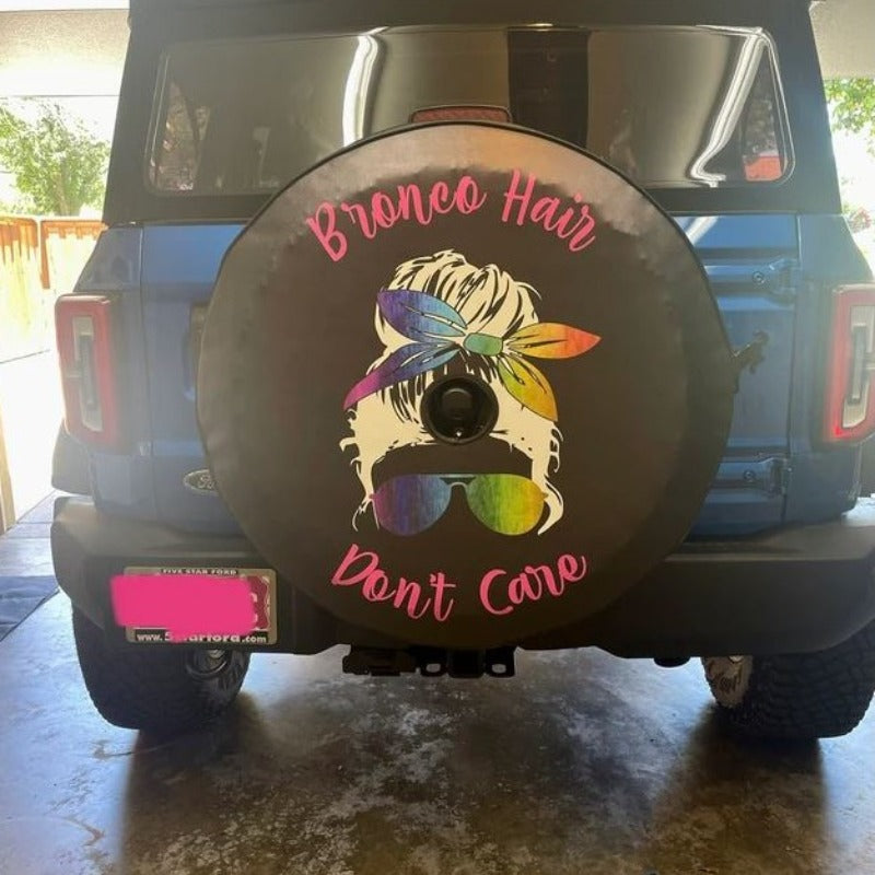 Bronco hair don't care saying with a silhouette of a girl with a messy bun wearing rainbow sunglasses and headband graphic on a spare tire cover for Ford Bronco 