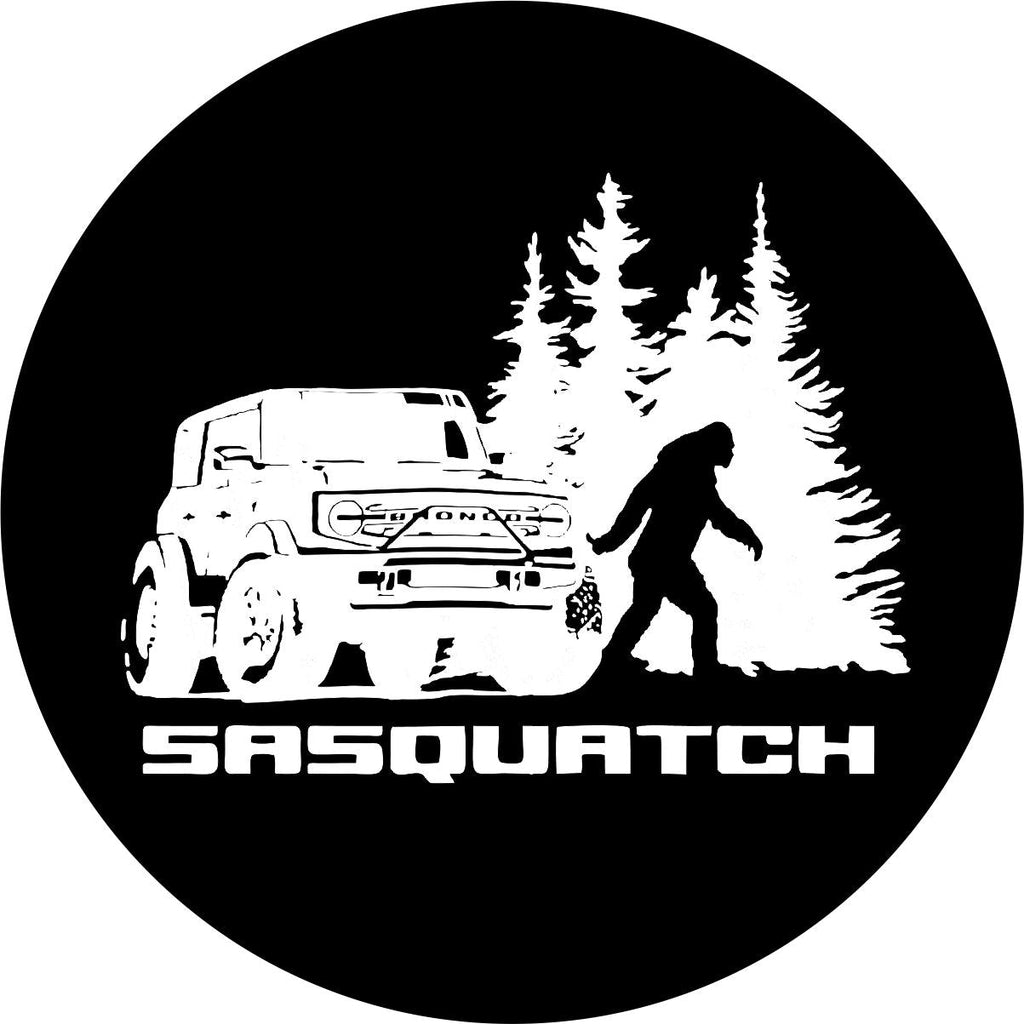 Bronco sasquatch tire cover in black or white vinyl with silhouette of sasquatch or bigfoot walking in the woods besides a Ford Bronco