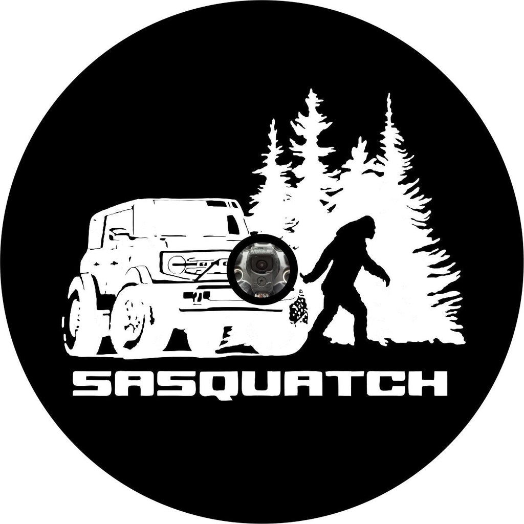 Bronco sasquatch tire cover in black or white vinyl with silhouette of sasquatch or bigfoot walking in the woods besides a Ford Bronco - design created for a back up camera