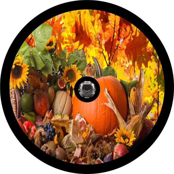 A spare tire cover with an image of a pumpkin, gourds, apples, sunflowers, and fall leaves with a place for a back up camera