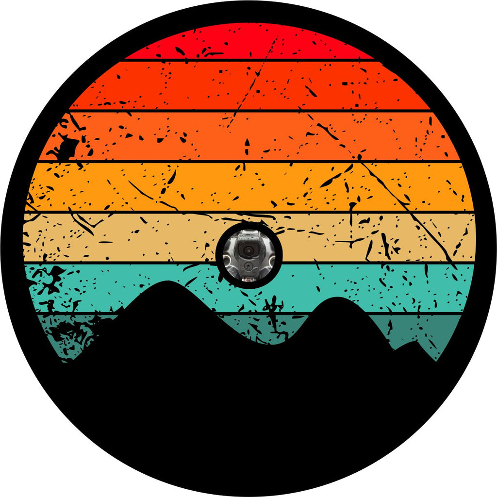 Red, orange, yellow, turquoise rustic stripes fill in the circle of this spare tire cover prototype design with the silhouette of mountains at the bottom and a space to fit a Jeep, Bronco, or other vehicle's spare tire that has a back up camera. 