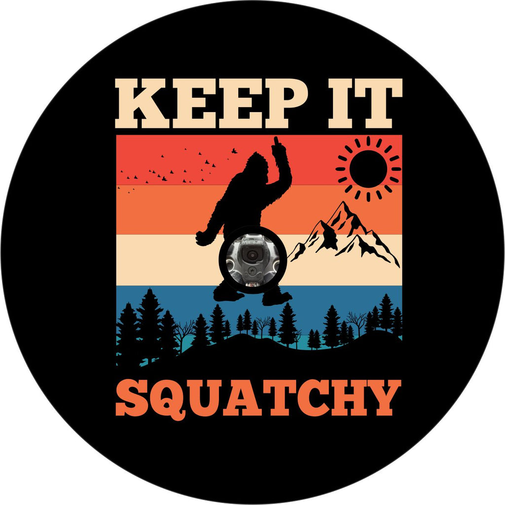 Black vinyl spare tire cover that says Keep It Squatchy, with a bigfoot silhouette giving the middle finger and a colorful mountain backdrop with a camera hole design for back up camera. 