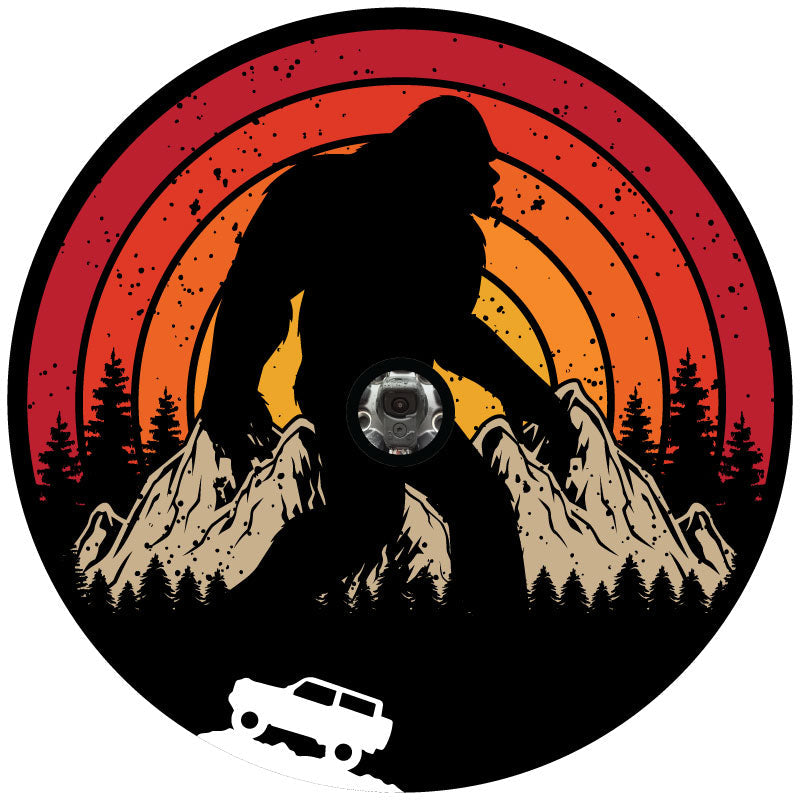 A retro vintage spare tire cover design with Sasquatch or bigfoot walking through the mountains and the silhouette of a Ford Bronco driving.  Designed for a black vinyl spare tire cover and a back up camera